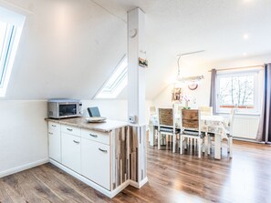 A modern kitchen with a microwave, wooden cabinets, and a dining area with a table and chairs. - Frankenblick by Interhome (Frankenau)
