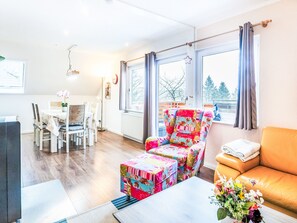 A modern living room with a sofa, a colorful armchair, a dining area with a table and chairs, and large windows with curtains. - Frankenblick by Interhome (Frankenau)