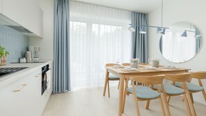 A modern kitchen with a dining area, featuring a large window with sheer curtains, a round mirror, and a wooden dining table set for four. - Wohnung für 6 Personen "Nowe Miedzywodzie" by Interhome (Miedzywodzie)
