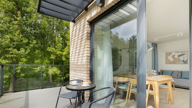 A modern outdoor patio with a glass wall, a round table with chairs, and a view of the interior dining area. - Wohnung für 6 Personen "Nowe Miedzywodzie" by Interhome (Miedzywodzie)