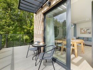 Un patio moderno al aire libre con pared de vidrio, una mesa redonda con sillas y vistas al área de comedor interior.