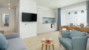 A modern living room with a sofa, a dining table with chairs, a kitchen area with cabinets, a flat-screen TV, and a large window with curtains. - Wohnung für 6 Personen "Nowe Miedzywodzie" by Interhome (Miedzywodzie)