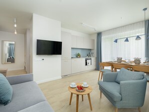 A modern living room with a sofa, a dining table with chairs, a kitchen area with cabinets, a flat-screen TV, and a large window with curtains. - Wohnung für 6 Personen "Nowe Miedzywodzie" by Interhome (Miedzywodzie)
