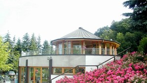 Ein zweistöckiges Gebäude mit Balkon, umgeben von üppigem Grün und rosa Blüten.