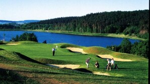 Ein Golfplatz mit einem See, Sandbunkern und einem bewaldeten Bereich.