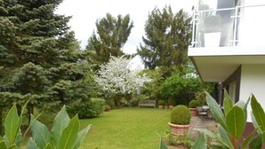 Ein gepflegter Garten mit Rasenfläche, verschiedenen Bäumen und einer Bank.