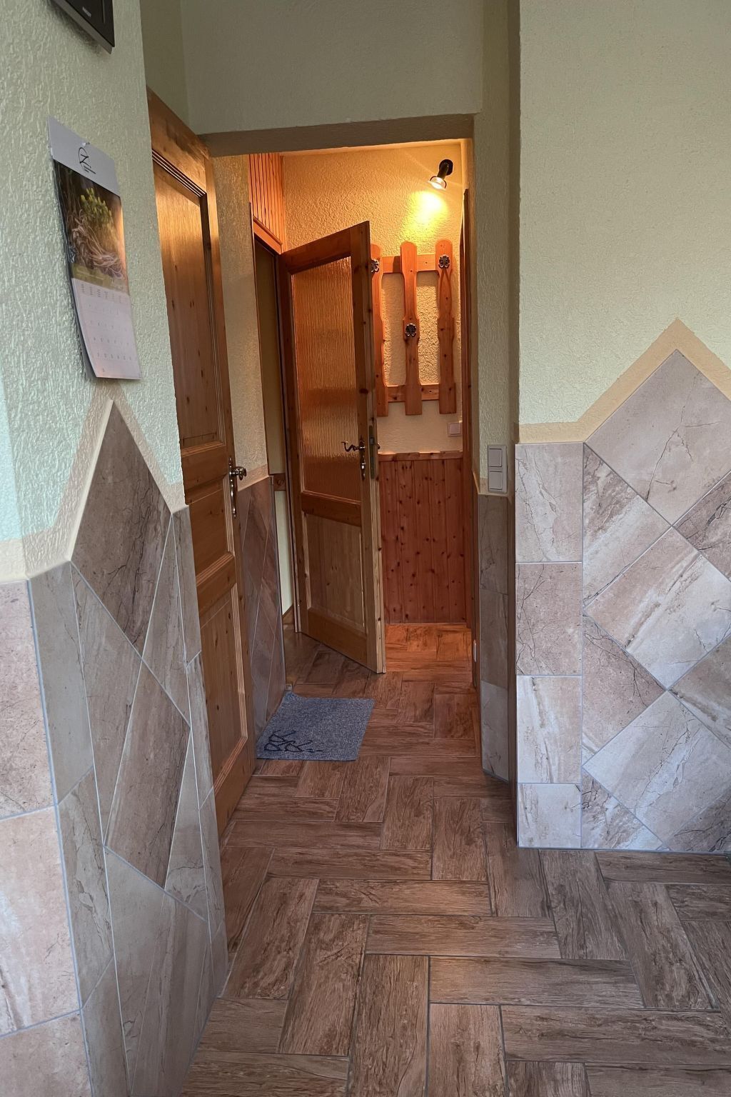Ein Korridor mit Holzboden, einer Holztür und einer gefliesten Wand.