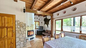 A rustic interior with a stone fireplace, wooden ceiling beams, and a large window offering a view of the outdoors.