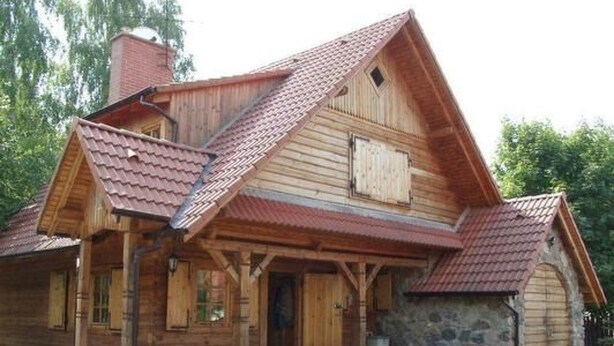 Una cabaña de madera con cimientos de piedra, un techo empinado y una chimenea.