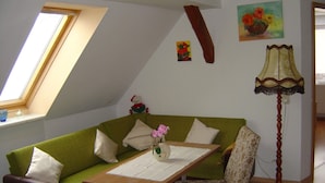 A cozy room with a green sofa, a wooden table, a chair, a lamp, and a painting on the wall.