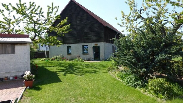 A large, dark-roofed building with a well-maintained lawn and a small shed to the left.