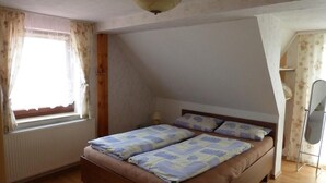 A bedroom with a bed, a window with curtains, a radiator, and a ceiling fan.