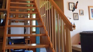 Una escala de fusta amb barana que condueix a una habitació amb escriptori, cadira i diversos objectes a la paret.