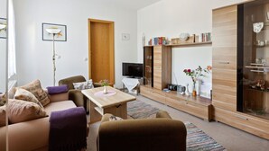 Un salon moderne comprenant un canapé, une table basse, un téléviseur et un meuble en bois doté de portes en verre.