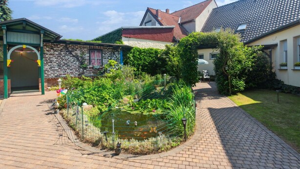 Une cour avec un bassin, un chemin en briques et un petit pont.
