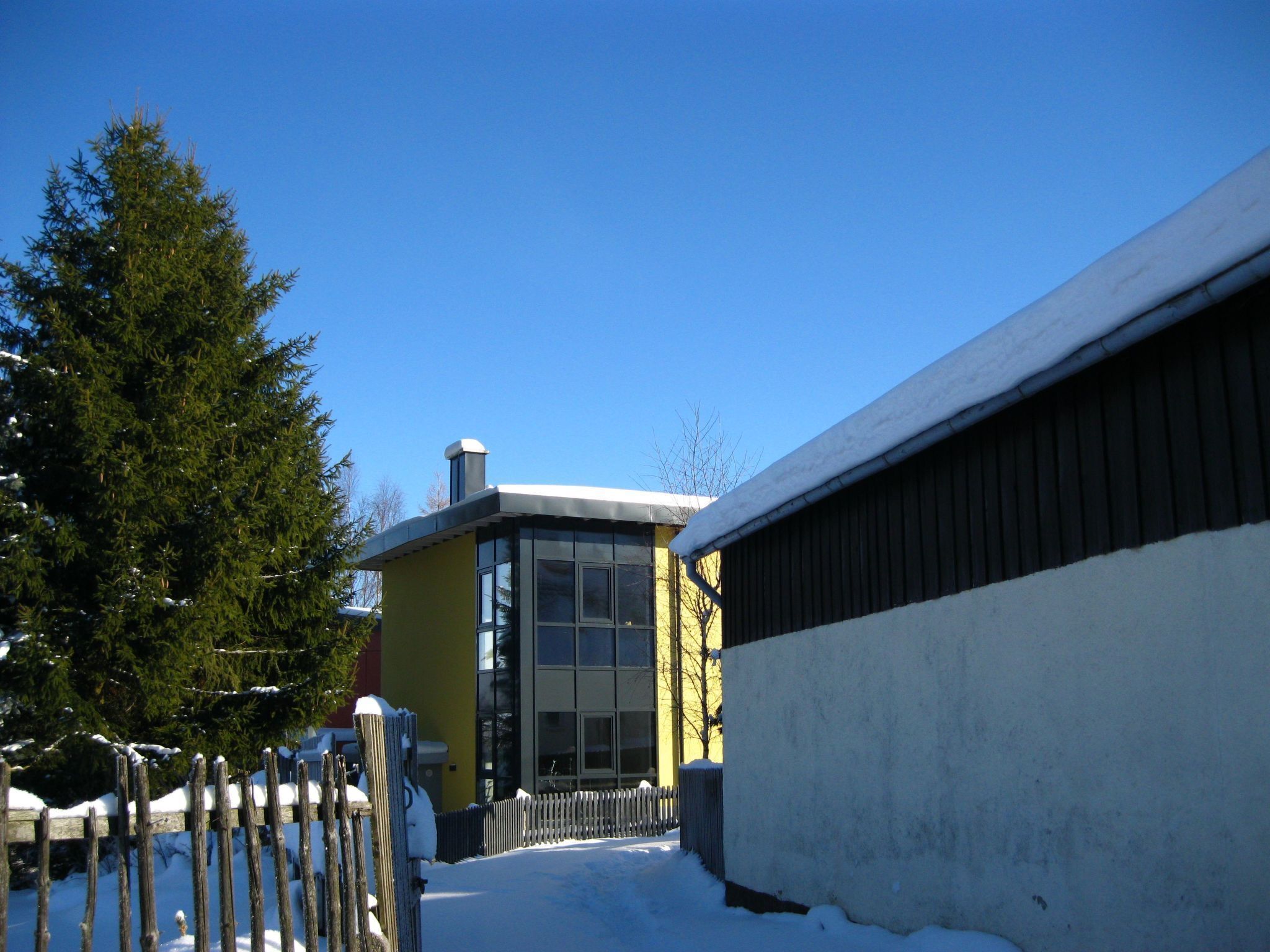 Un bâtiment enneigé, doté d’une façade jaune et de grandes fenêtres, entouré de neige et d’une clôture en bois.