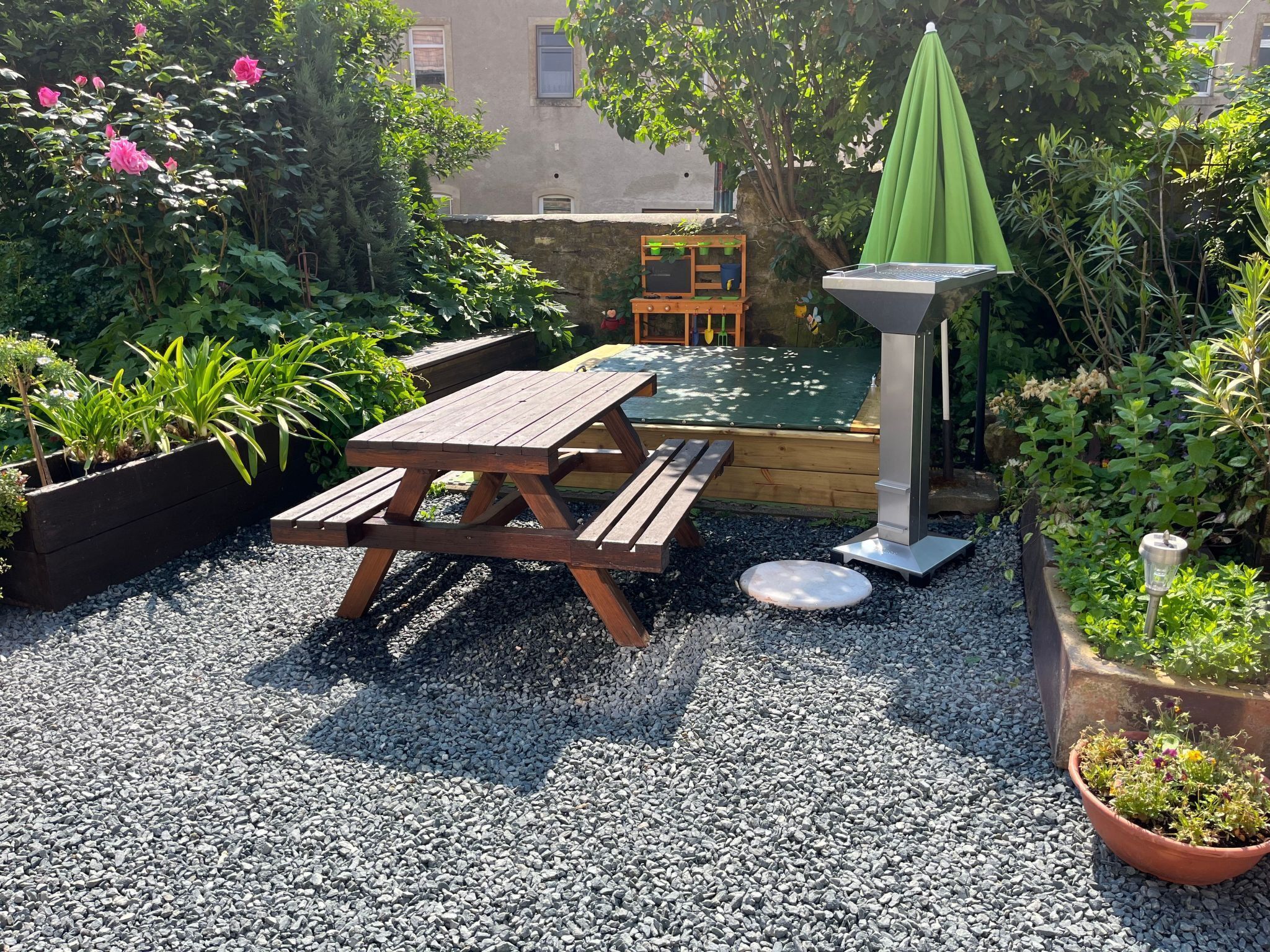 A wooden picnic table with benches, surrounded by gravel, and a green umbrella.