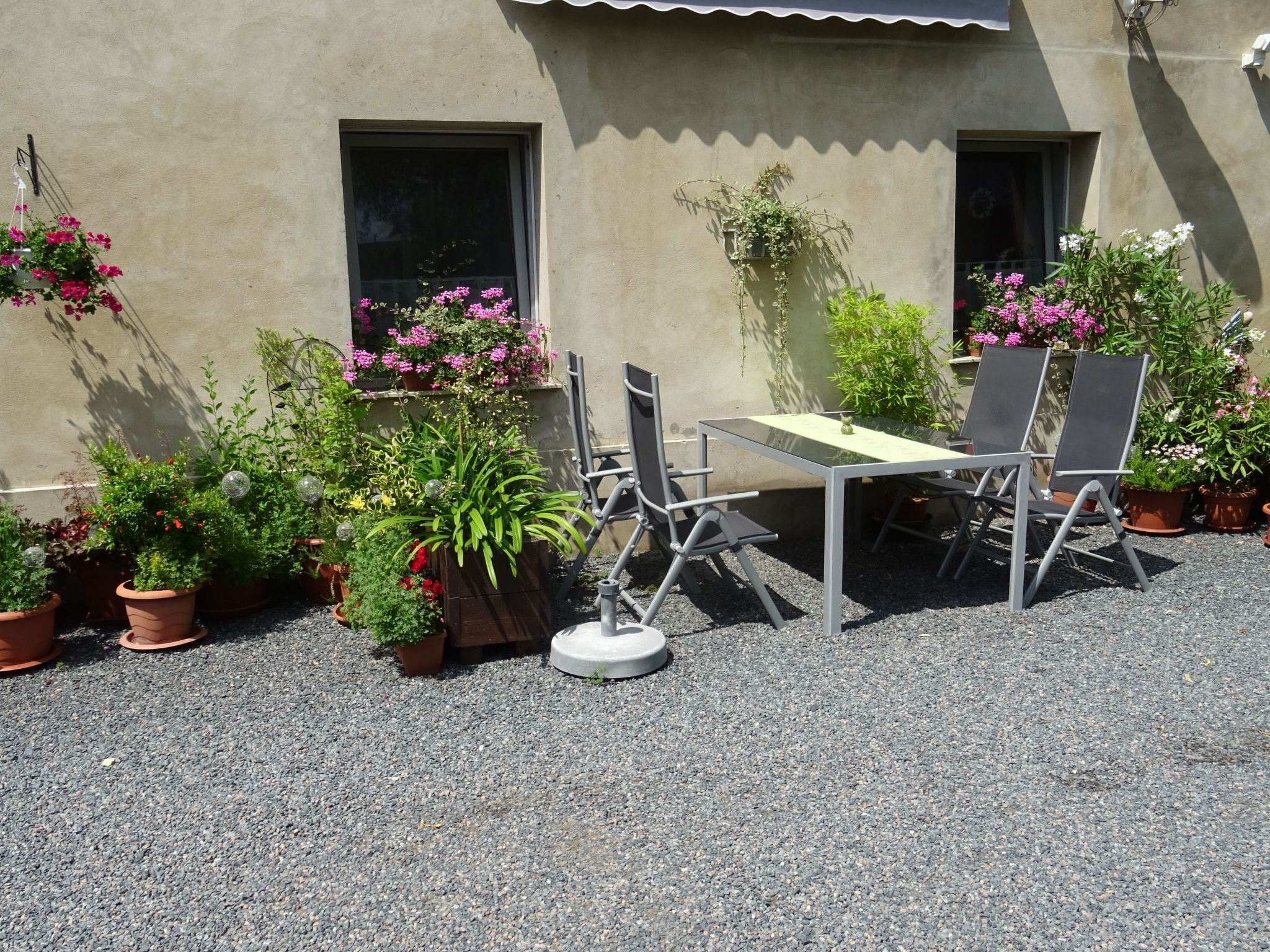 Eine Terrassengruppe mit Tisch und Stühlen, umgeben von Blumentöpfen und Blumen.
