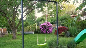 Un jardín con un columpio, un tobogán verde y diversas plantas y flores.