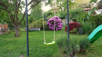 A garden with a swing set, a green slide, and various plants and flowers.