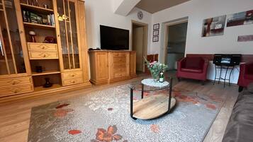A living room with a wooden cabinet, a flat-screen TV, a glass coffee table, and a red sofa.