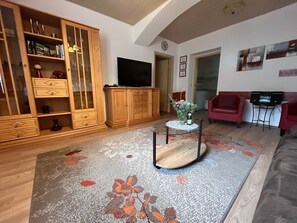 Ein Wohnzimmer mit Holzschrank, Flachbildfernseher, Glastisch und einem roten Sofa.