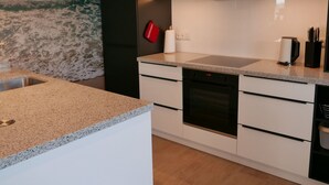 Une cuisine moderne dotée d’un plan de travail en granit, d’un évier en acier inoxydable, d’un four noir et de meubles de rangement blancs.