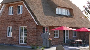 Un bâtiment en briques surmonté d’un toit de chaume et doté d’un patio avec des sièges en plein air.