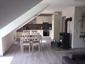 A modern kitchen with white cabinets, a dining table with chairs, a black stove, and a lofted sleeping area. - Apartment Möwe by Interhome (Baabe)