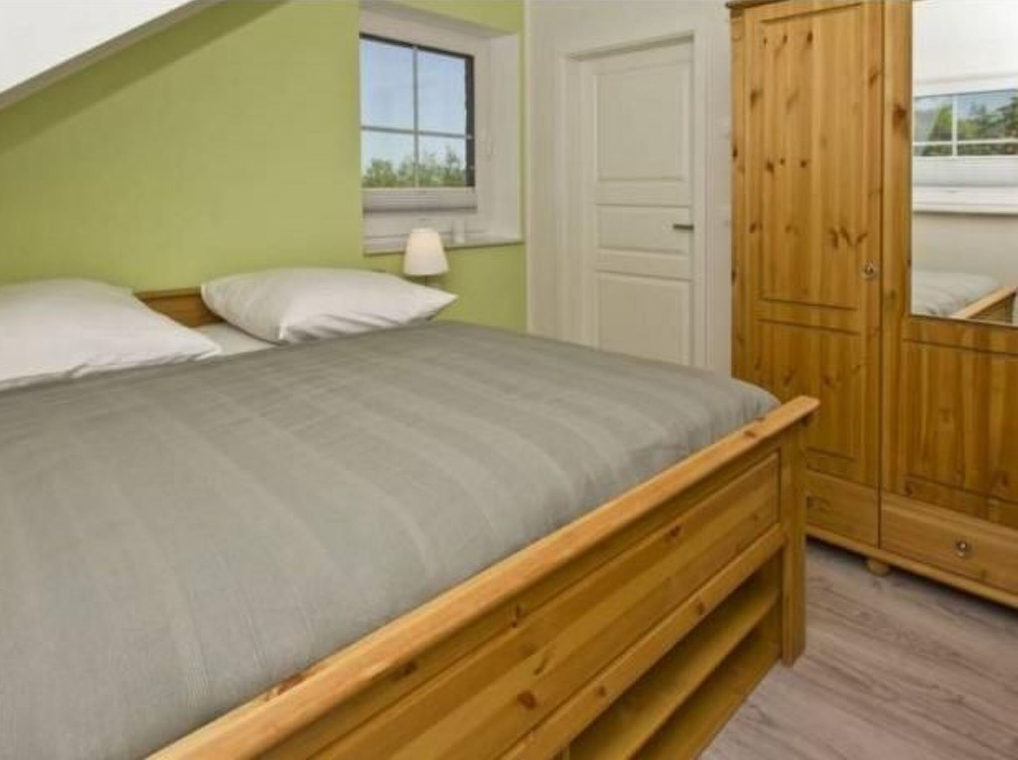 Une chambre à coucher avec un lit, une armoire en bois, une fenêtre et une porte.