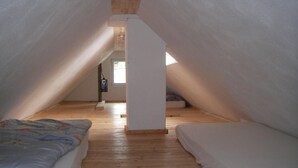 A high-ceilinged attic bedroom with wooden floors and two beds.