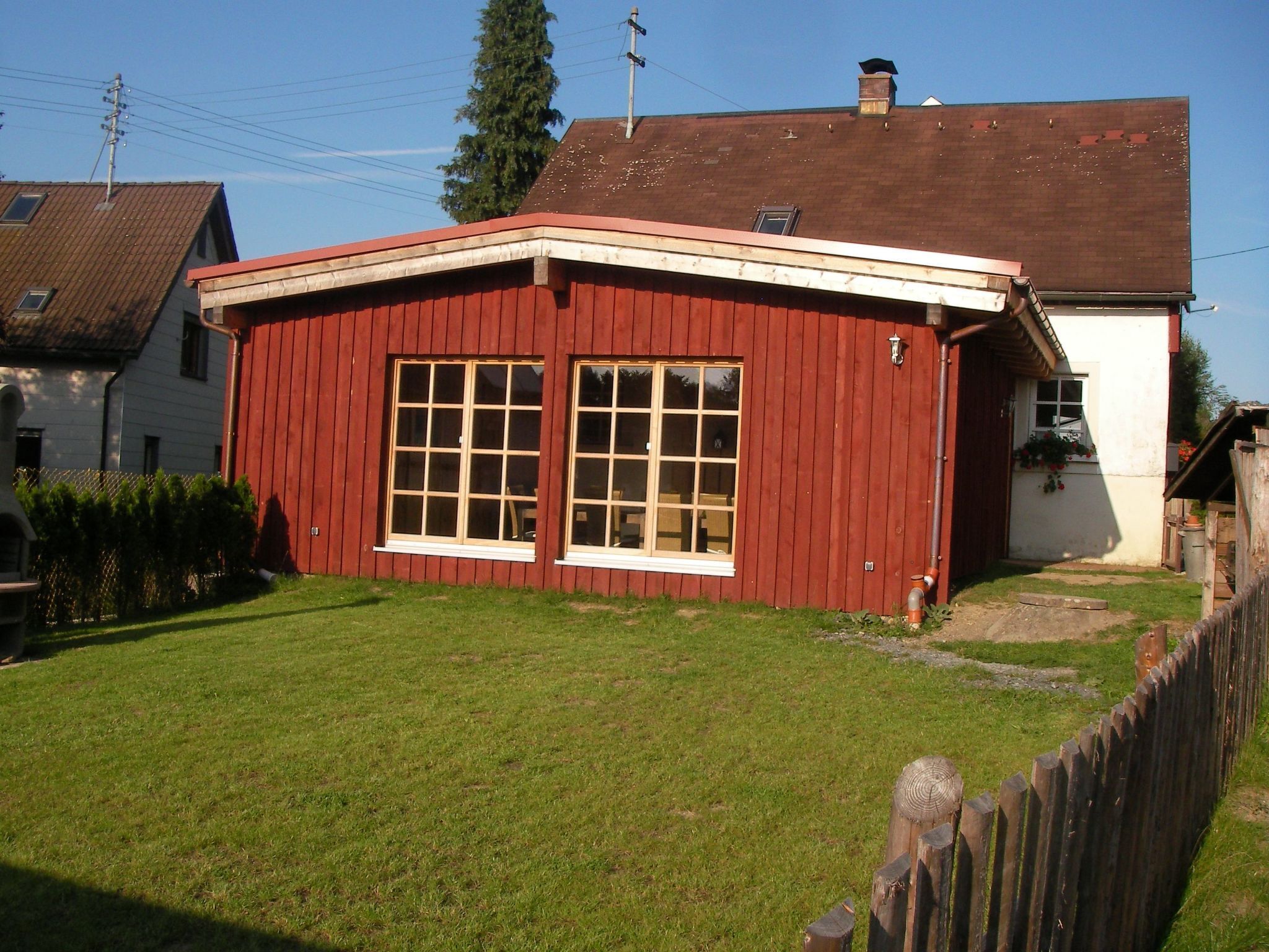 A red wooden house with a white exterior, a large window, and a small porch.
