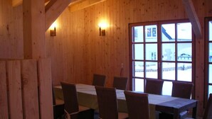 A wooden interior with a dining table and chairs, large windows, and wooden walls.