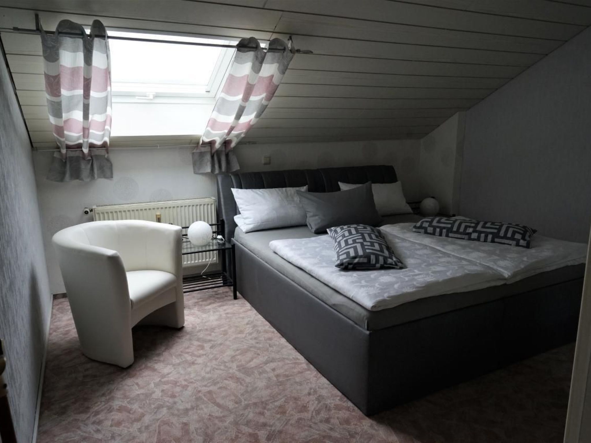 A bedroom with a bed, a chair, a radiator, and curtains.