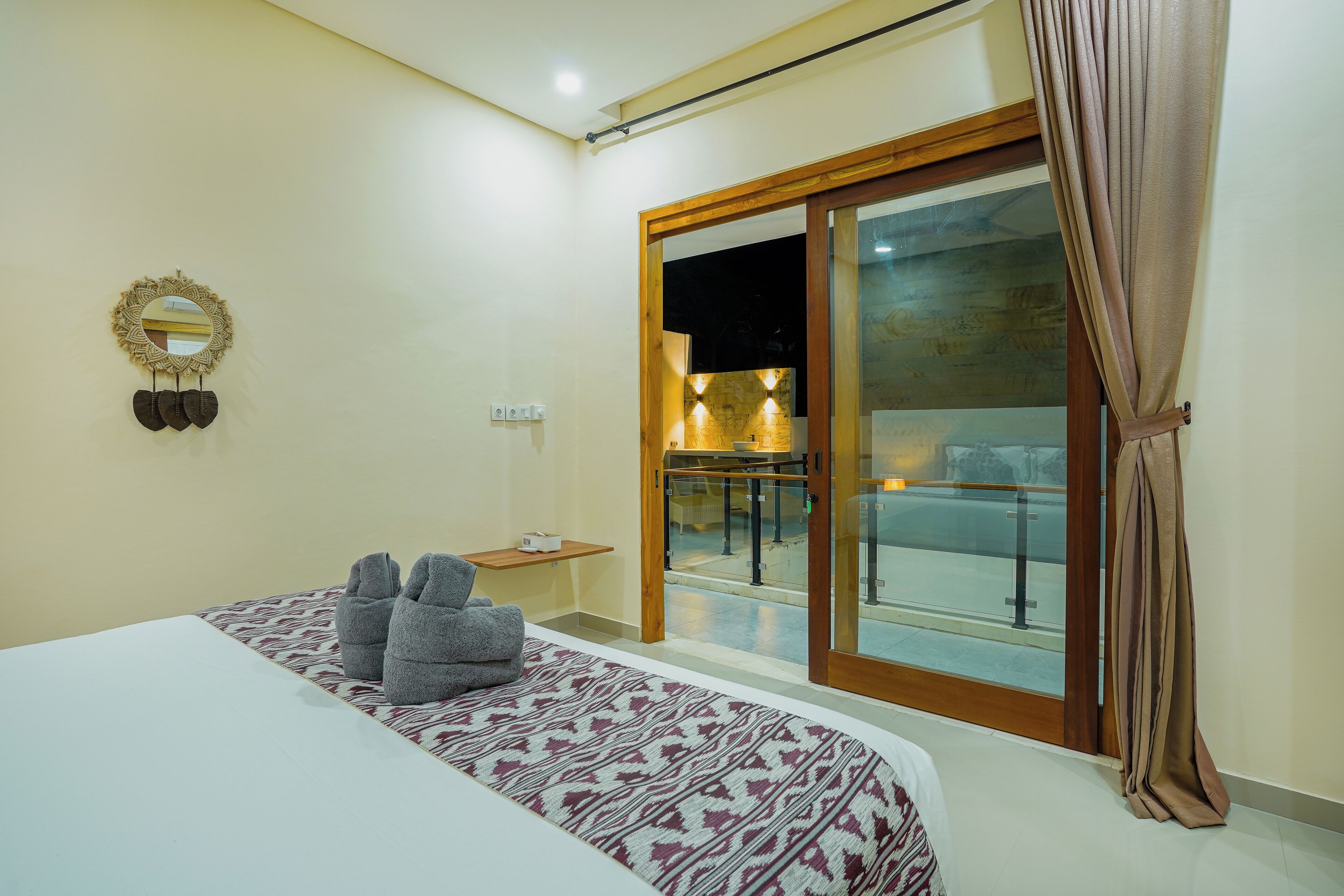 Habitación de hotel con una cama, una mesita pequeña, un espejo en la pared y una puerta corrediza de vidrio que da a un área exterior.