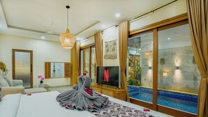 A spacious bedroom with a large bed, a television, a sliding glass door to a pool, and a ceiling fan. - 3-bedroom Private pool villa City Sanur (Denpasar)