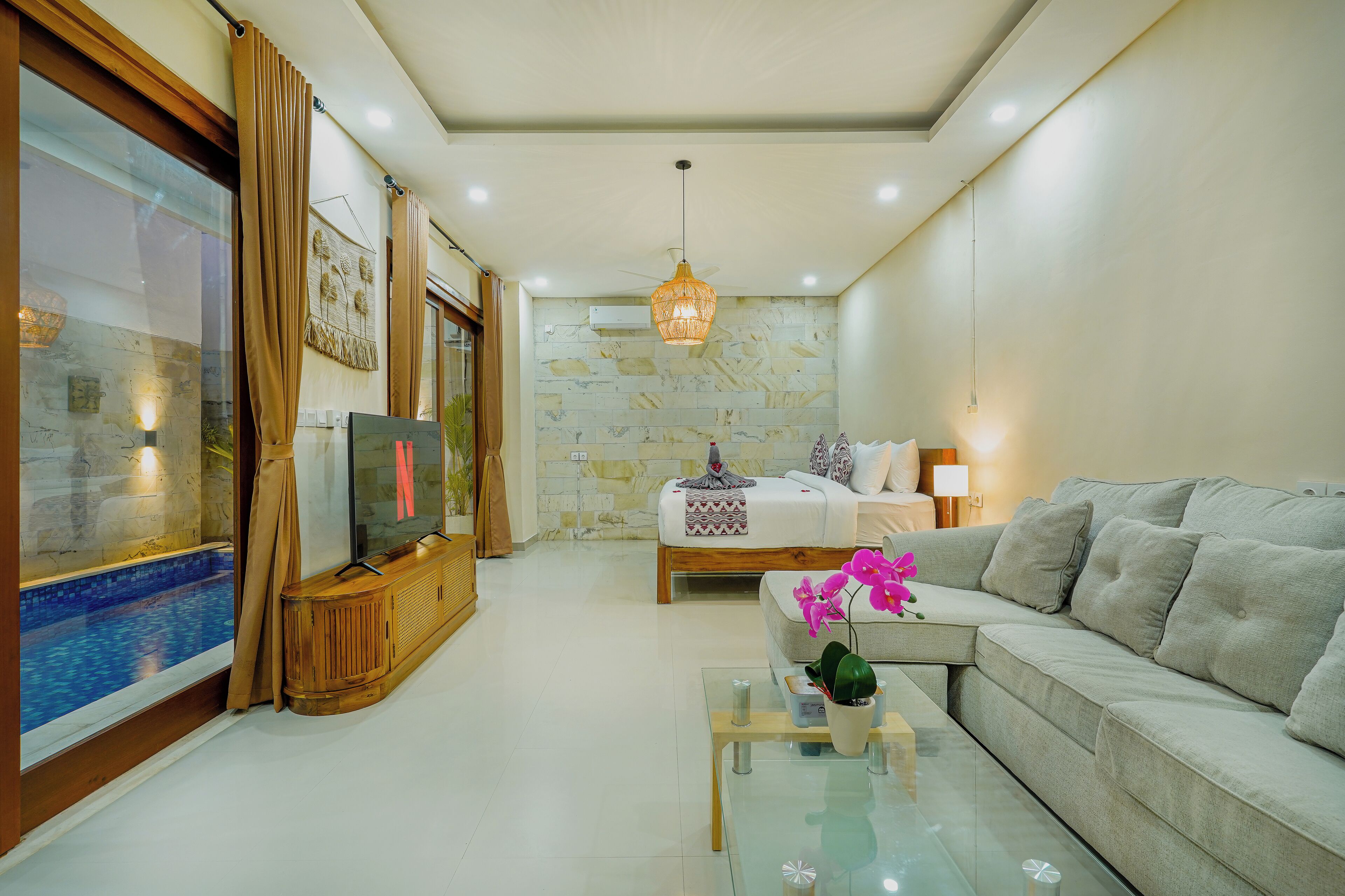 A modern living room with a sofa, a glass coffee table, a TV, and a stone wall.