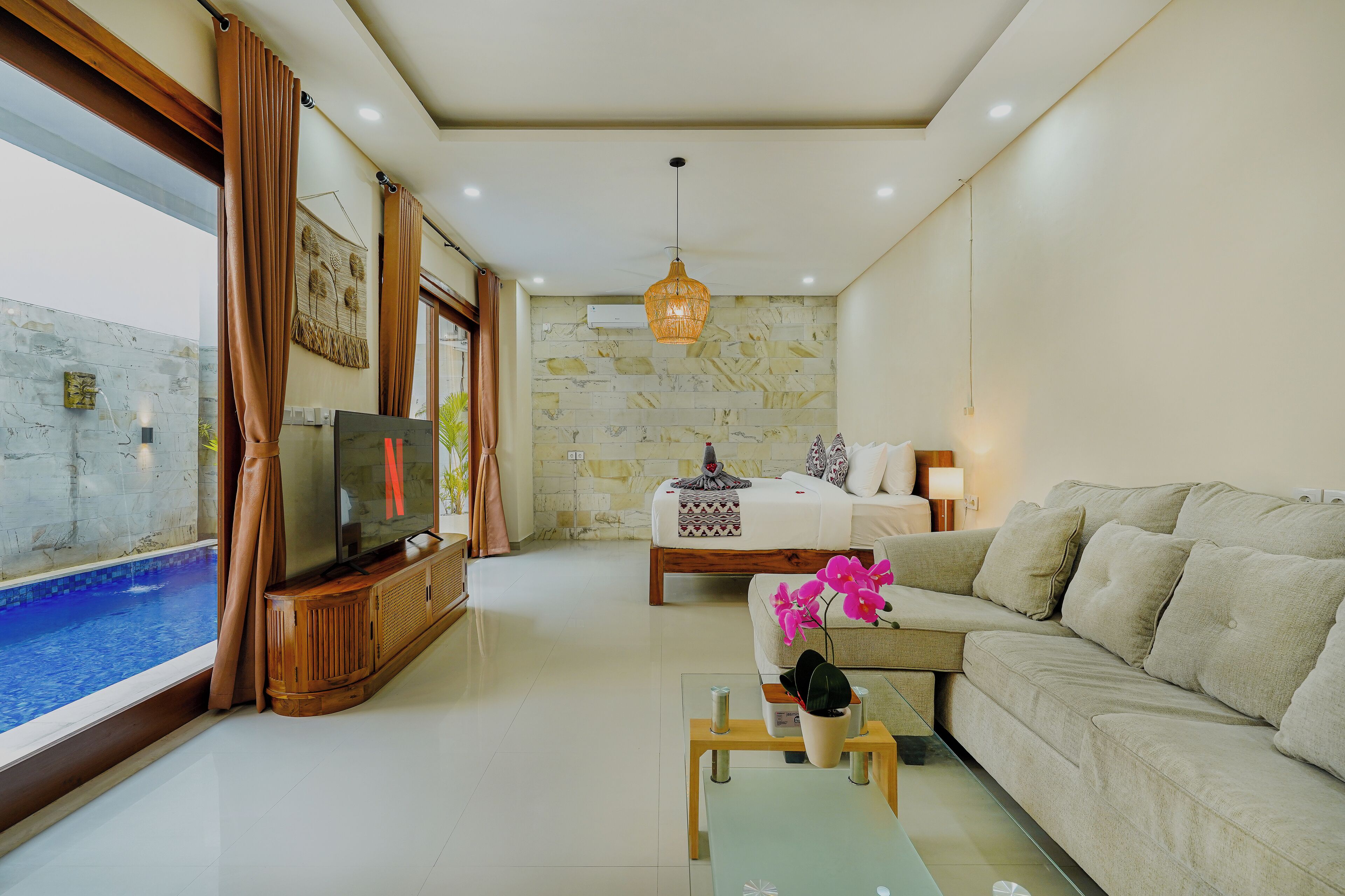 A modern living room with a TV, sofa, coffee table, and a view of a swimming pool.