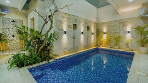 An indoor swimming pool with a tiled floor, surrounded by plants and stone walls. - 3-bedroom Private pool villa City Sanur (Denpasar)