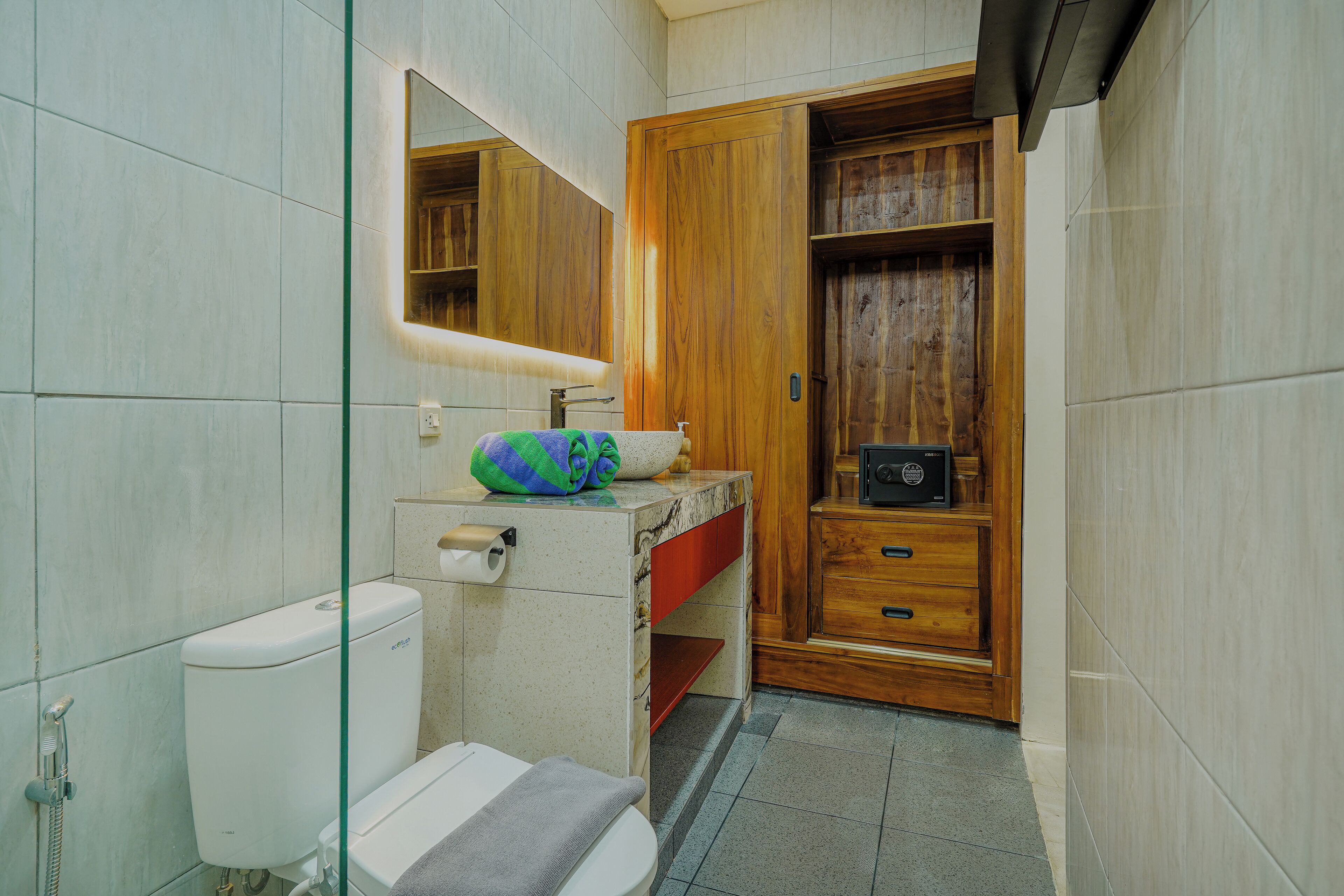 A bathroom with a toilet, sink, mirror, and wooden cabinet.