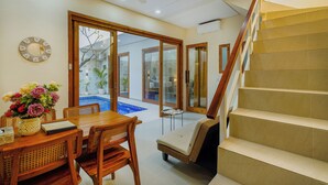 A spacious living area with a wooden dining table, chairs, and a sofa. A staircase leads to an upper level. - 3-bedroom Private pool villa City Sanur (Denpasar)