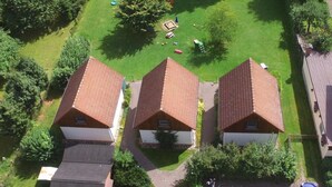 A residential area with three houses, each with a sloped roof and a small front yard. There is a paved driveway leading to the houses, and a person is visible walking on the driveway. - Haus im Grünen by Interhome (Marktgraitz)