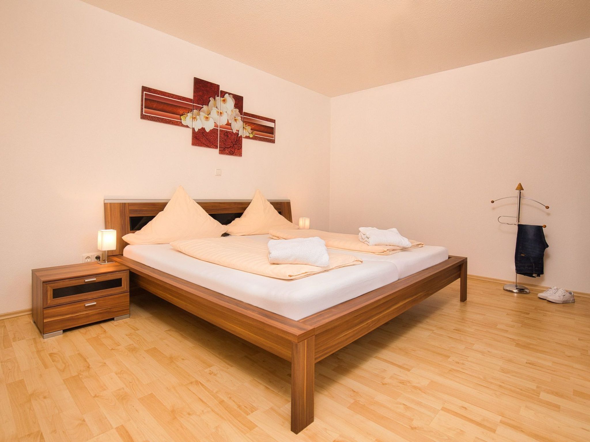 Une chambre d’hôtel bien rangée, avec un lit en bois, des tables de chevet, une lampe et une œuvre d’art accrochée au mur.