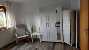 Una habitación con cama, una silla, una mesita, un armario y un radiador.