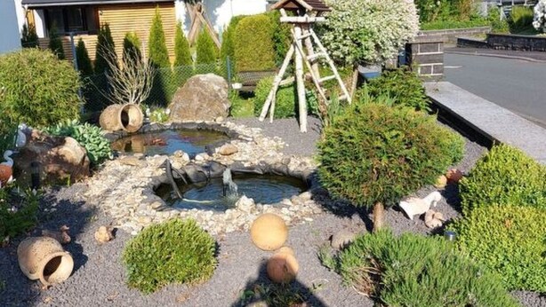 Un jardín con un estanque, rocas y una estructura de madera.