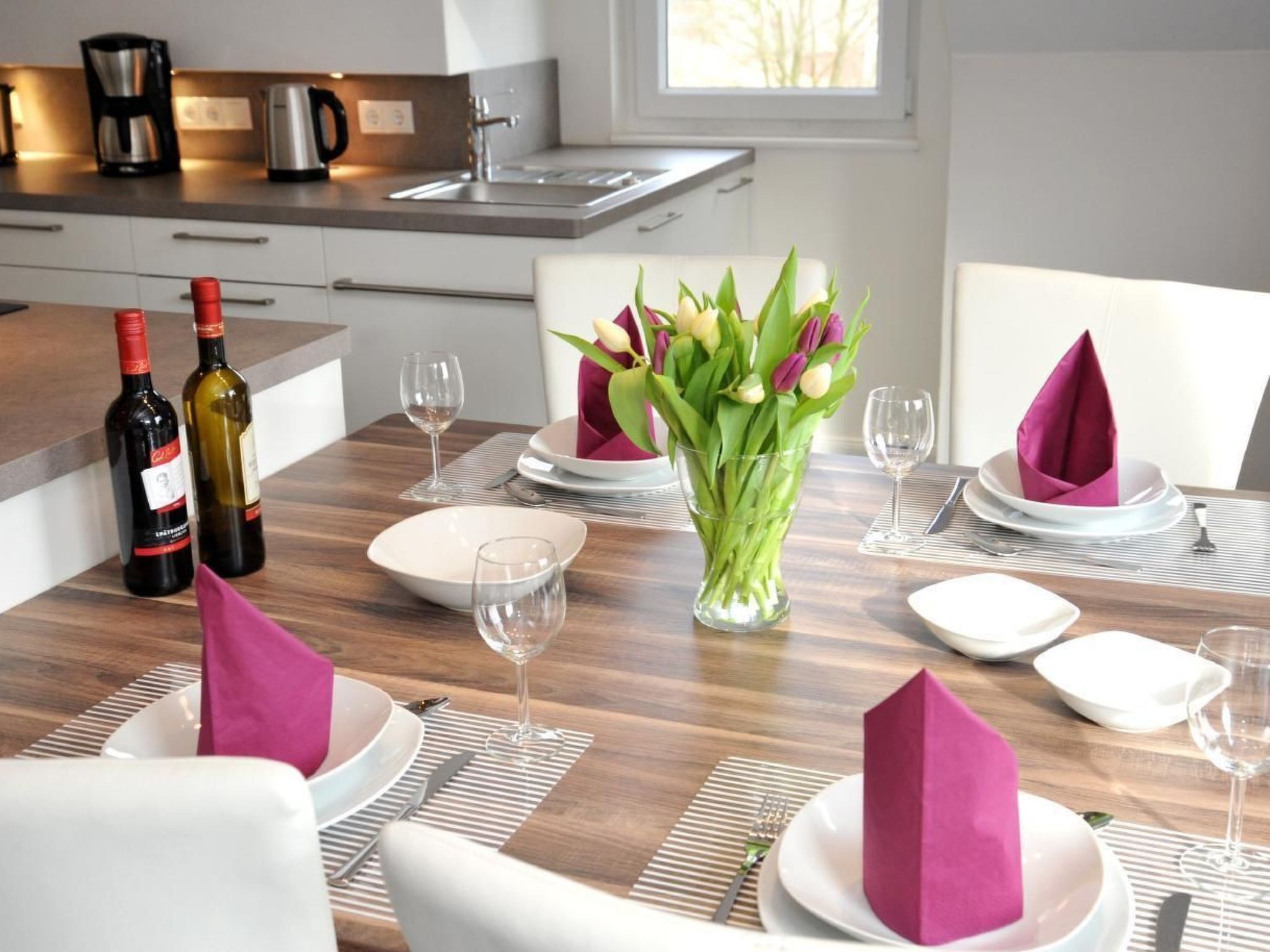 A dining area with a wooden table set for four, including plates, glasses, and napkins.