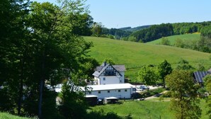 A white house with a sloped roof, surrounded by lush green fields and trees. - in Feldmannshof mit Grill und Garten by Interhome (Drolshagen)