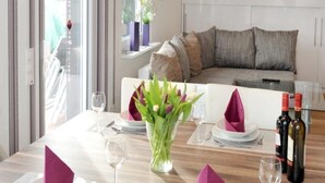 A dining area with a wooden table set for four, white chairs, and a vase of flowers. - in Feldmannshof mit Grill und Garten by Interhome (Drolshagen)