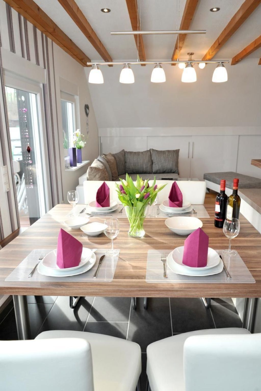 A dining area with a wooden table set for four, white chairs, and a vase of flowers.