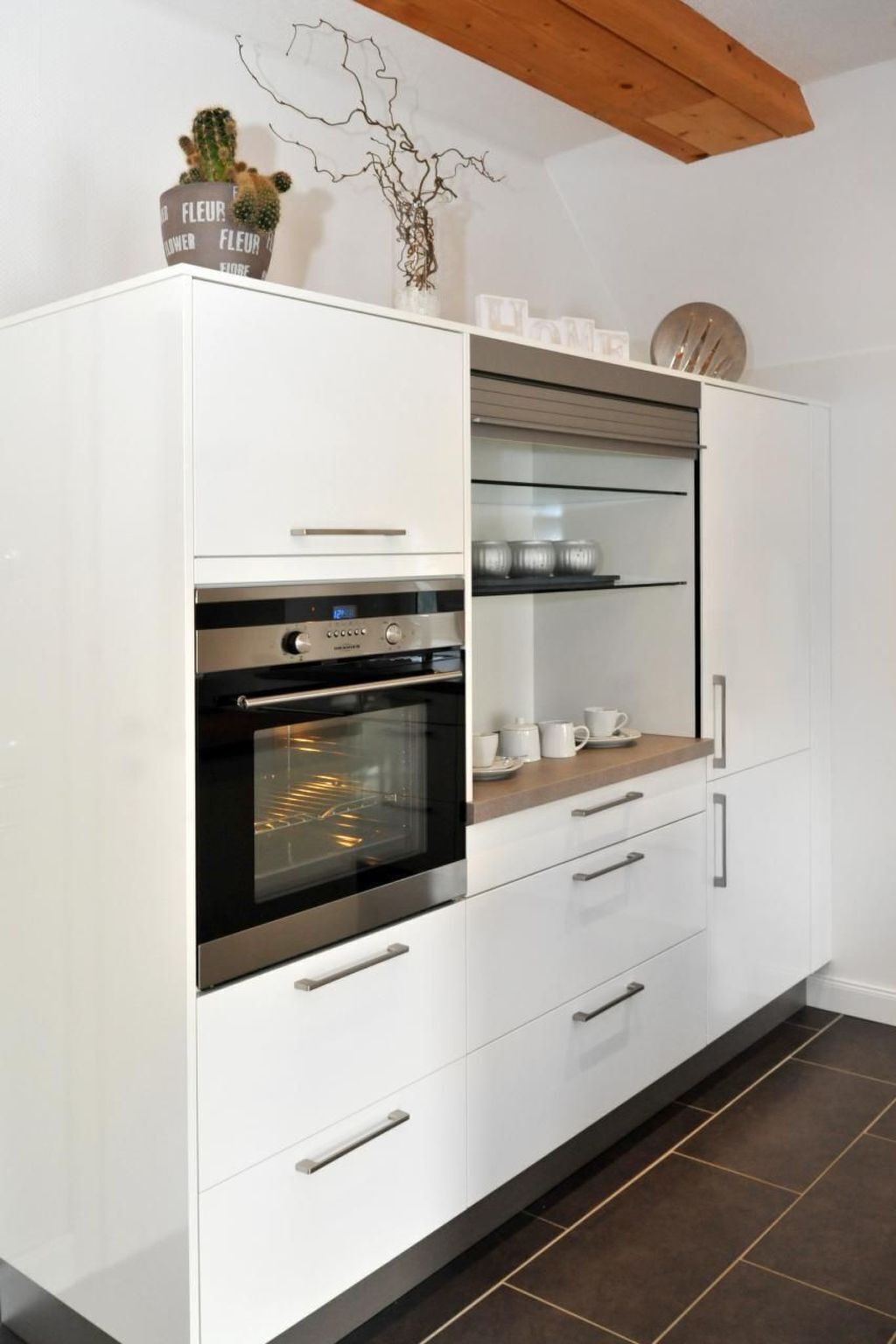 A modern kitchen with white cabinetry, a built-in oven, and a glass-fronted upper shelf.